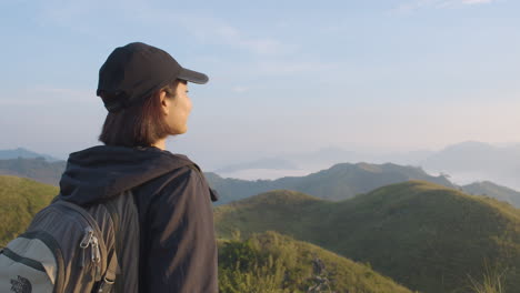 side shot of a young woman in cap breathing fresh air on top of a mountain