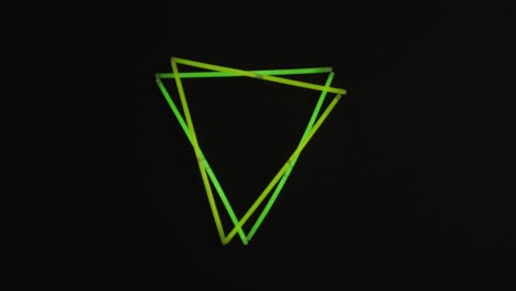 animation of green neon glow sticks forming triangles over black background with copy space