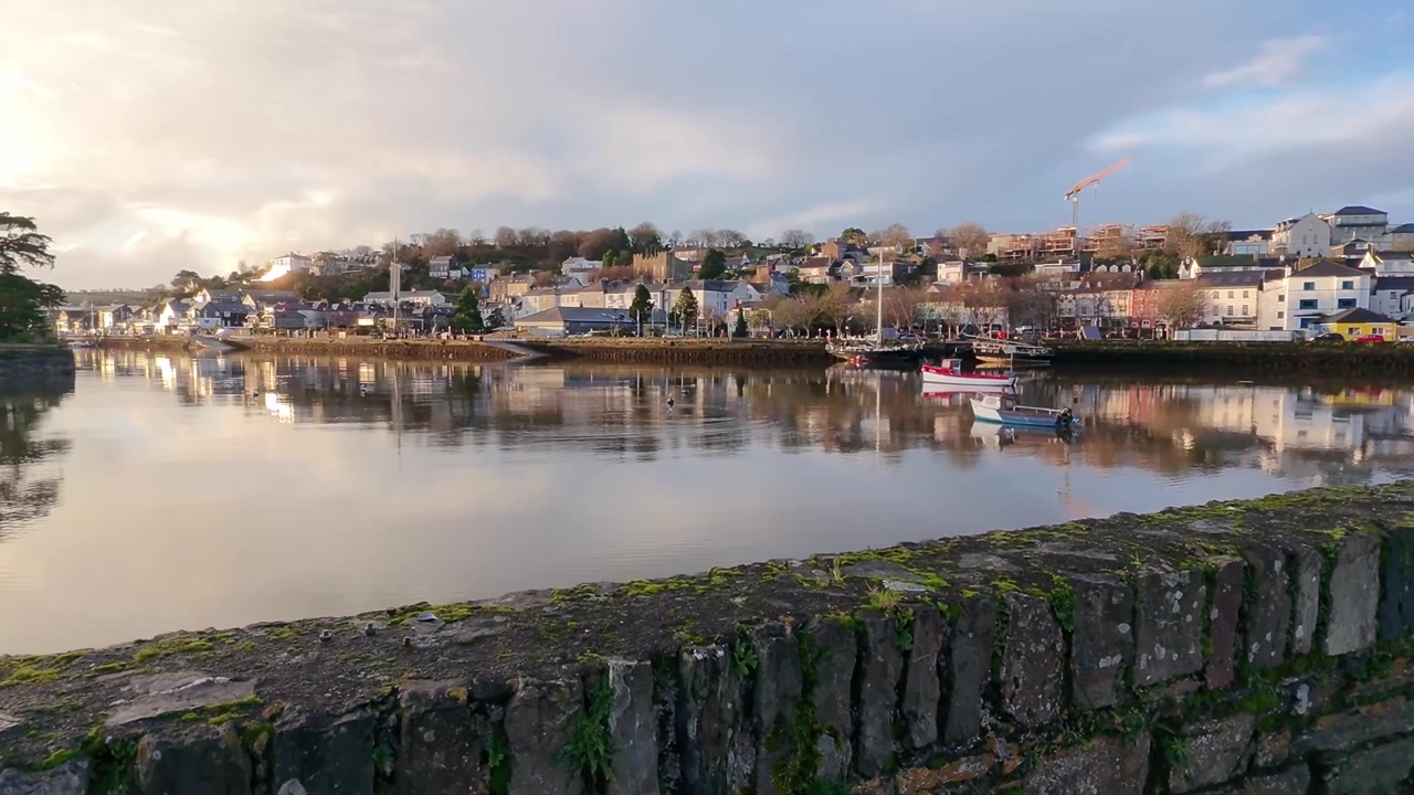 Reflejos en el agua, pueblo costero y dron aterrizando detrás de un muro de piedra en Kinsale, Irlanda.