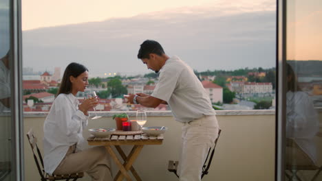 un marido cariñoso sirviendo mesa en el balcón del hotel. una pareja joven cenando románticamente.