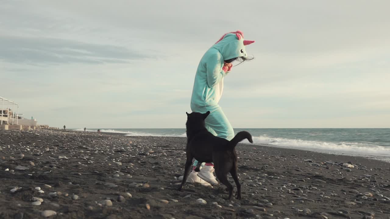 유니콘 의상 을 입은 여자 가 해변 에서 개 와 함께 놀고 있다