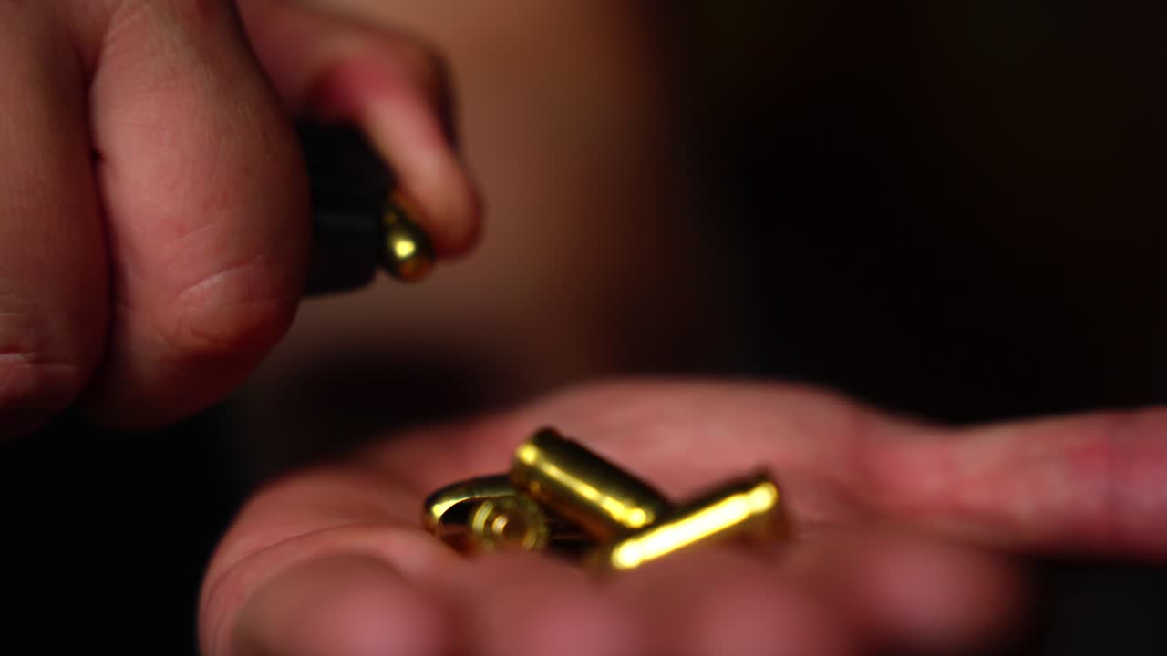 Close-up of hand unloading pistol magazine in low light with shallow focus on bullets flicked out of magazine