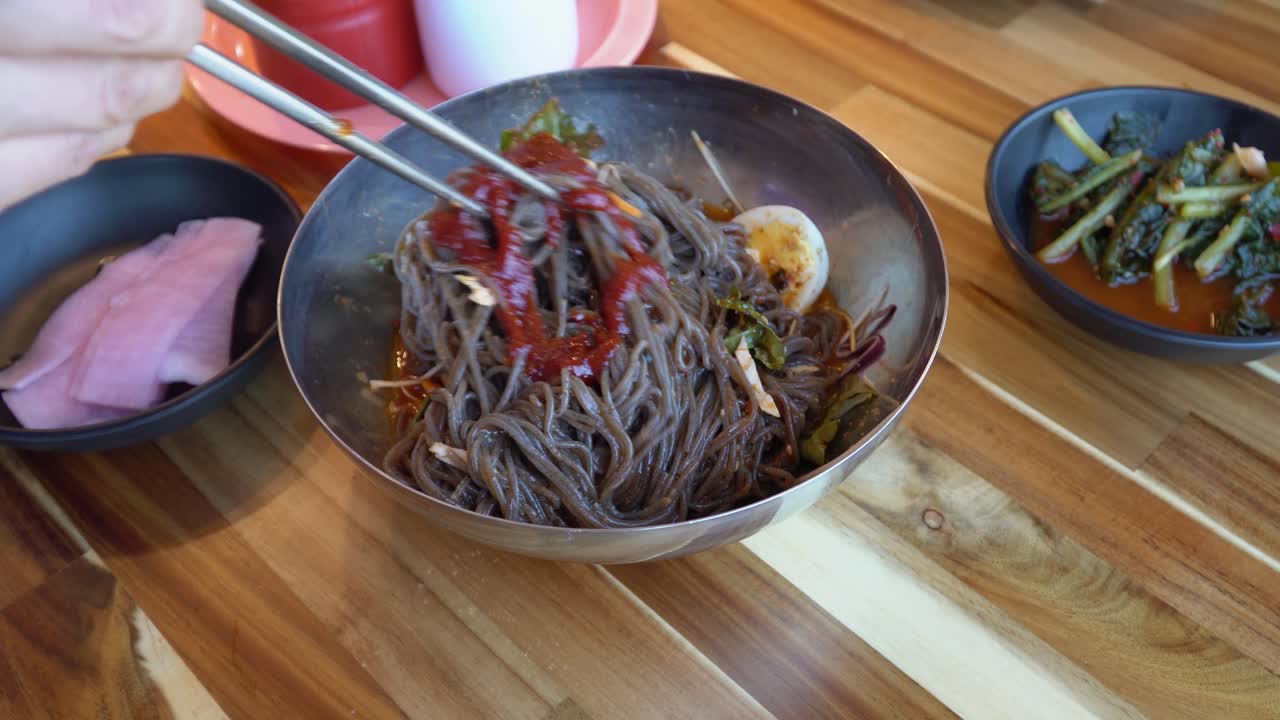 agregando gochujang a los fideos coreanos de trigo sarraceno y mezclándolos con palillos - ciudad de chuncheon, corea del sur - primer plano, ángulo alto