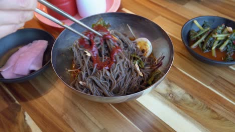 adding gochujang to korean buckwheat noodles and mix with chopsticks - chuncheon city, south korea - close up, high angle