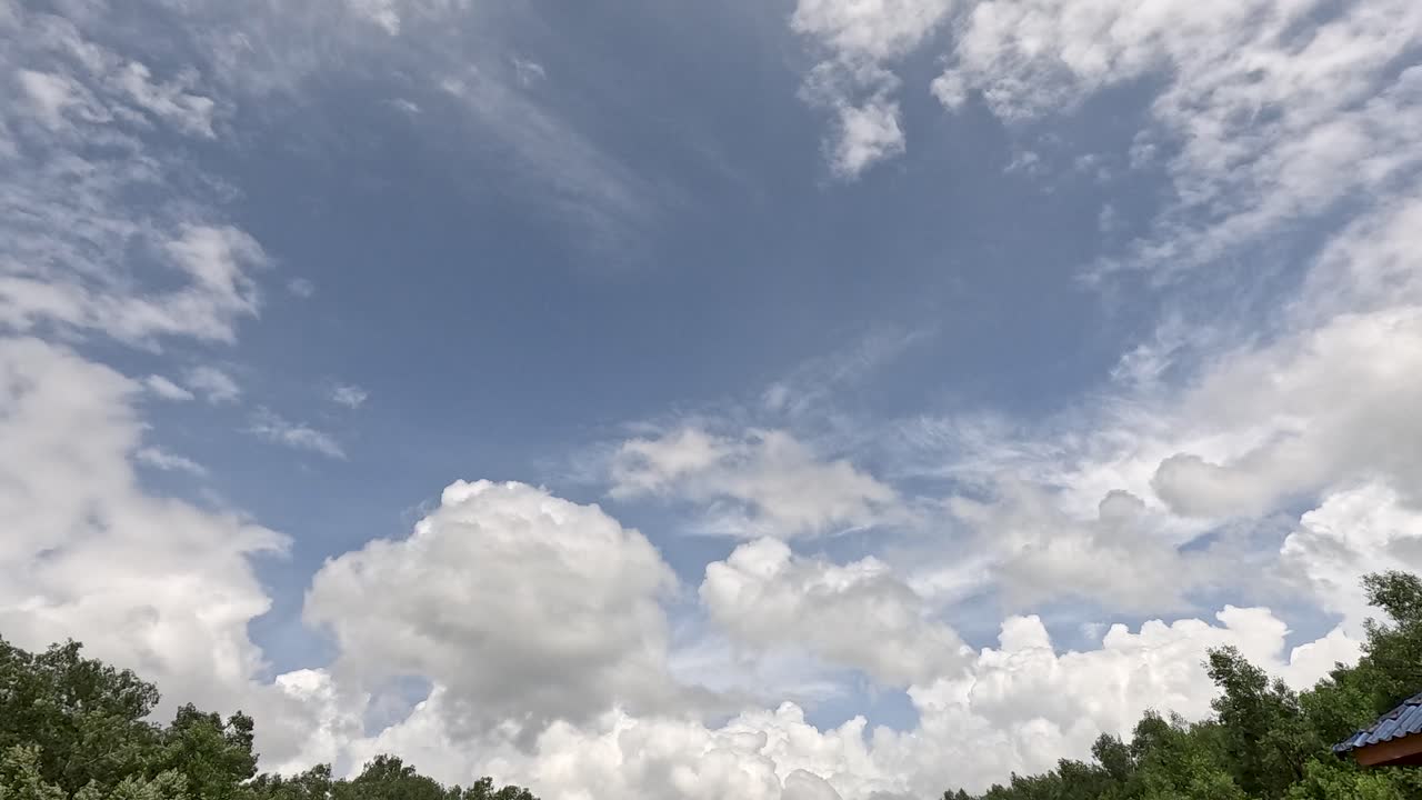 White cumulus clouds drift across a blue sky above lush green treetops in daylight, captured with a stationary camera in Ko Phayam, Thailand