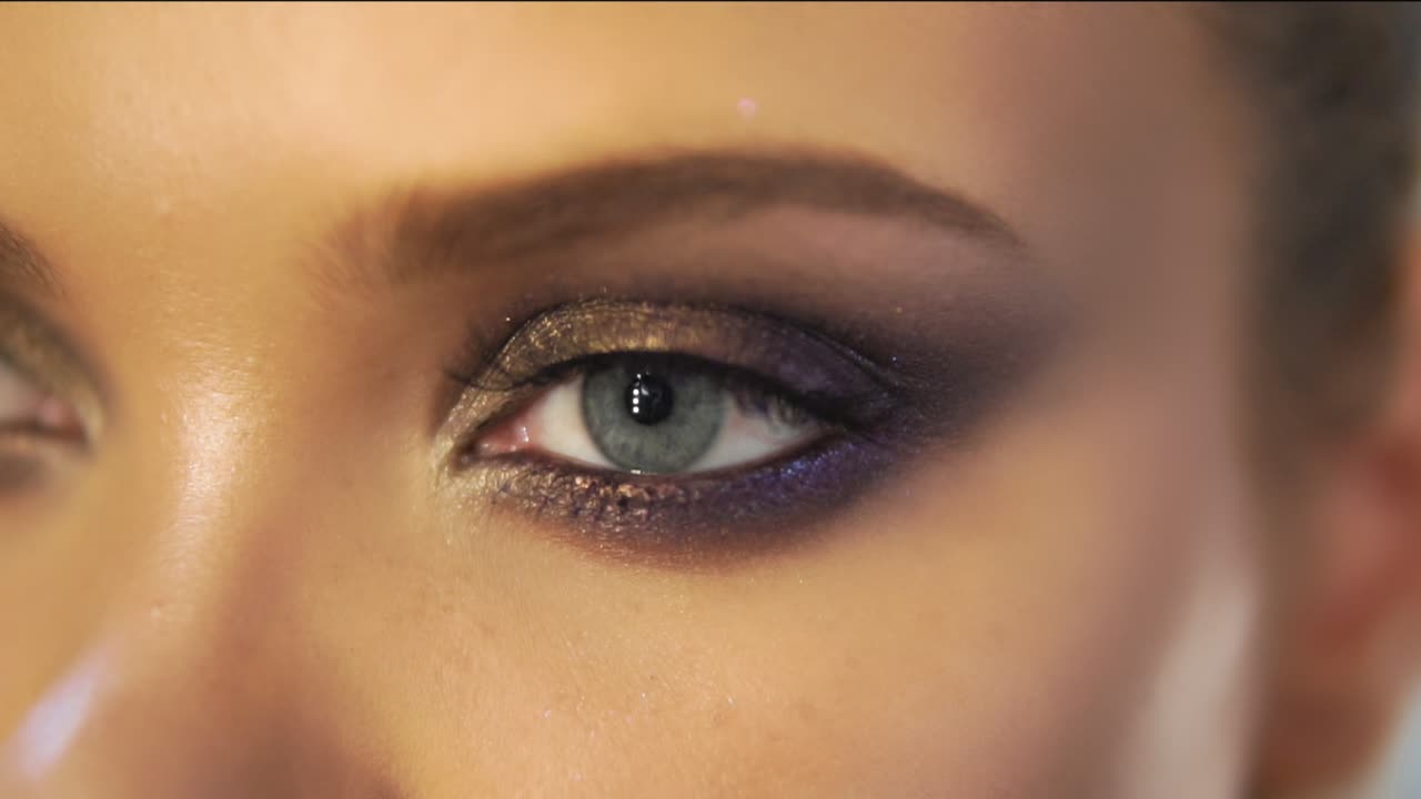 Close Up view of woman's eyes with beautiful golden makeup opening in Slow Motion