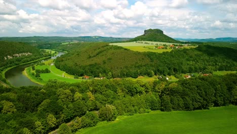 Iconic-Mountain-top-in-Saxony-filmed-by-drone-at-high-altitude-from-afar-with-vies-on-the-green-country-side-and-River-Elbe-in-eastern-Germany-with-graded-skies-and-clouds