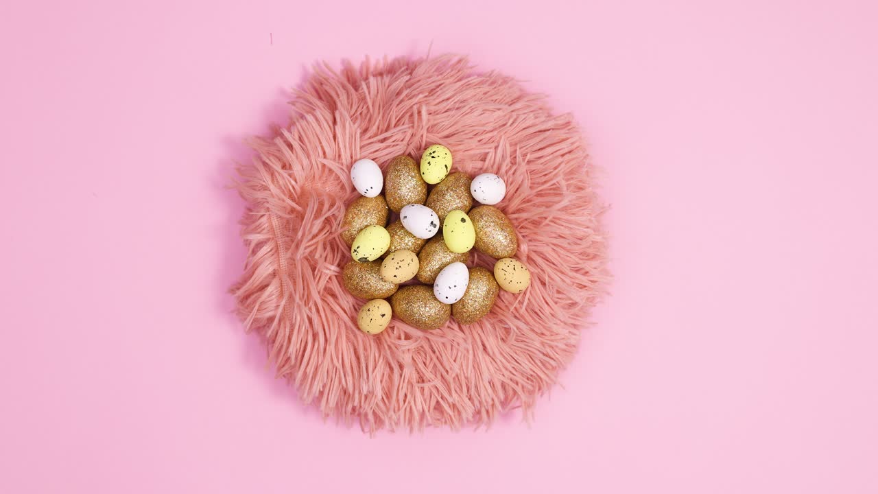 Easter glamour gold eggs appear in fur nest on pastel pink background. Stop motion flat lay