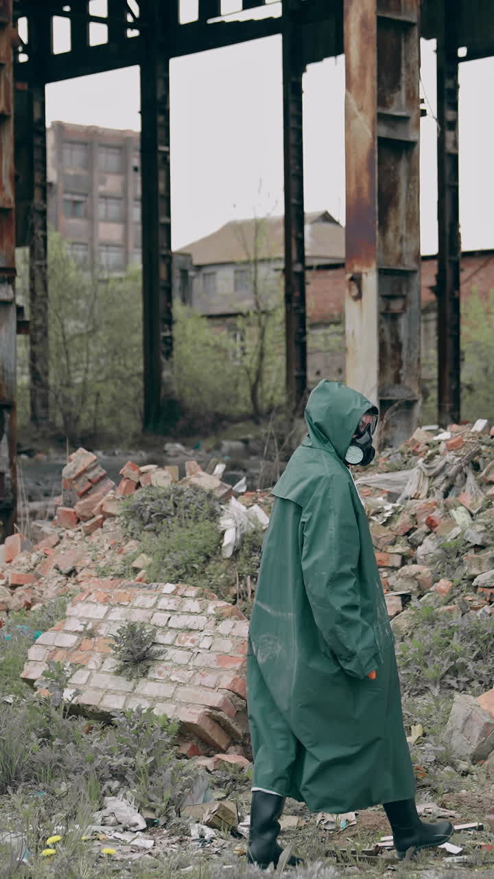 Person in chemical protective suit walking in distracted place. Survivor in abandoned place with piles of garbage from ruined buildings. Apocalypse concept. Vertical video