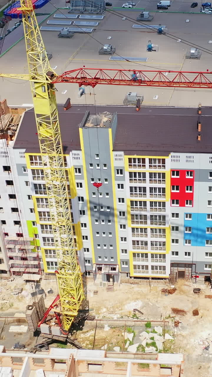 Construction of a multi-storey apartment building. Building of a multi-quarter houses in the city. Tower crane on a construction site. Aerial view. Vertical video