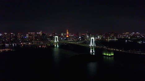 Vista-Aérea-Subiendo-En-El-Puente-Del-Arco-Iris-En-La-Noche-Sobre-El-Agua