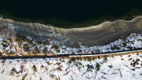 toma en cámara lenta de un tren rojo que pasa por las playas del lago kamloops durante la hora dorada arrojando sombras largas, escena increíble del entorno del desierto cubierto de nieve