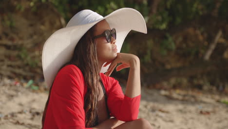 latin woman daydreams on beach, wearing red dress and white hat, portrait shot