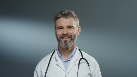 portrait shot of the handsome gray haired male doctor in the white gown and with stethoscope on his neck smiling cheerfully to the camera