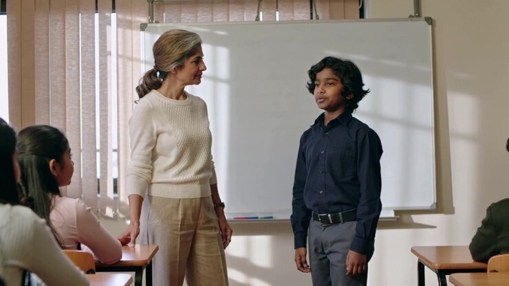 Male student answering question after teacher cream sweater asking at front class, with whiteboard