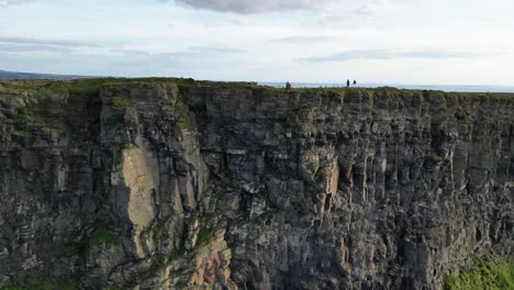 drone flying away from the cliffs of moher while people stand and hike along the ridge at sunset