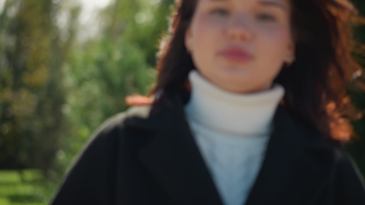 나무의 스에 앉아있는 여자의 클로즈업, 그녀의 머리카락이 바람에 부드럽게 불어, 조용한 공원 환경에서 울창한 초록색으로 둘러싸여, 평온하고 평화로운 분위기를 불러일으킨다.