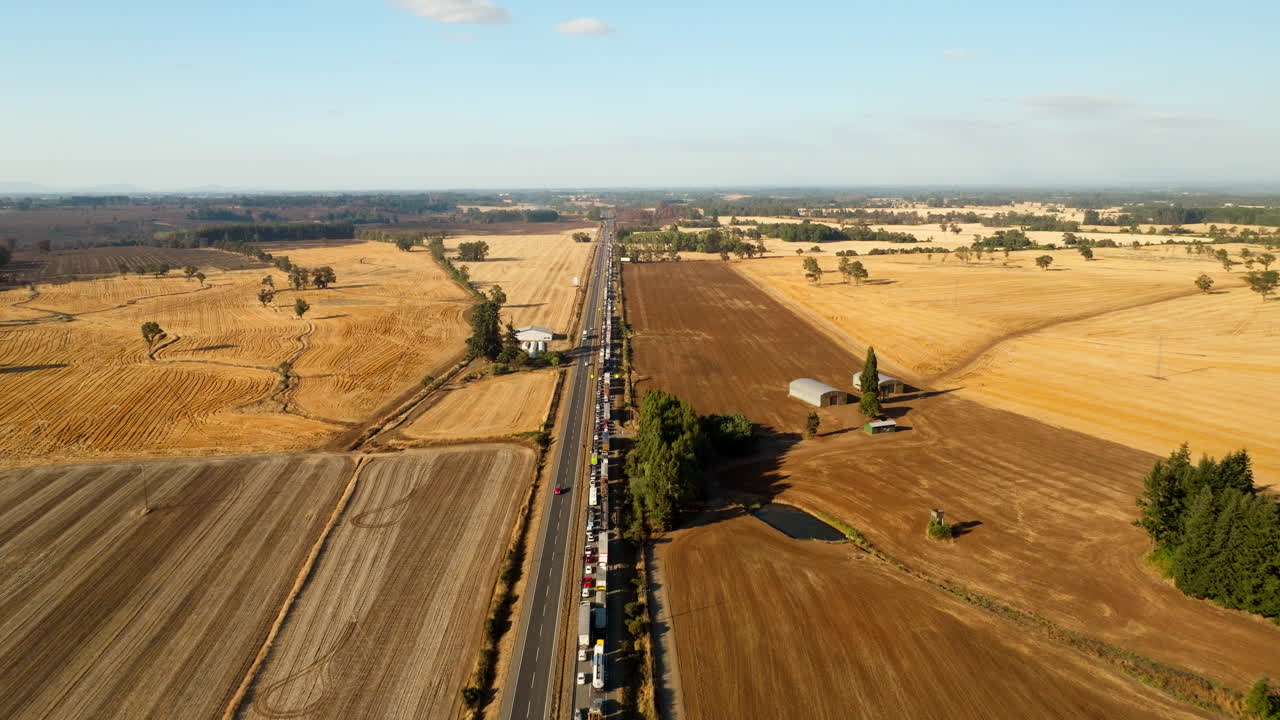Traffic jam on rural highway, long line of stationary cars and trucks in scenic countryside, cultivated fields, Chile. Aerial forward