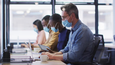 office colleagues wearing face masks working while sitting on their desks at modern office