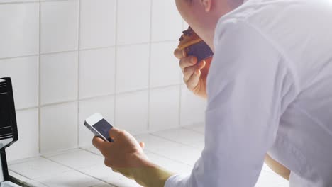 man using mobile phone while having muffin in kitchen 4k
