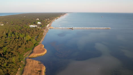 Aerial-landing-shot-of-jetty-and-scenic-coastline-of-Hel-Island-with-underwater-plants-at-sunset