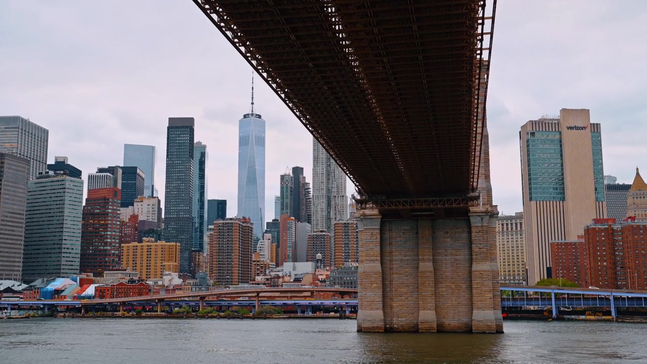New York, USA, 25 maggio 2026: Sottostruttura e pilastro in muratura del Ponte di Brooklyn a New York. Travatura reticolare in acciaio del ponte che guarda verso lo skyline di Manhattan attraverso l'acqua in una giornata nuvolosa.