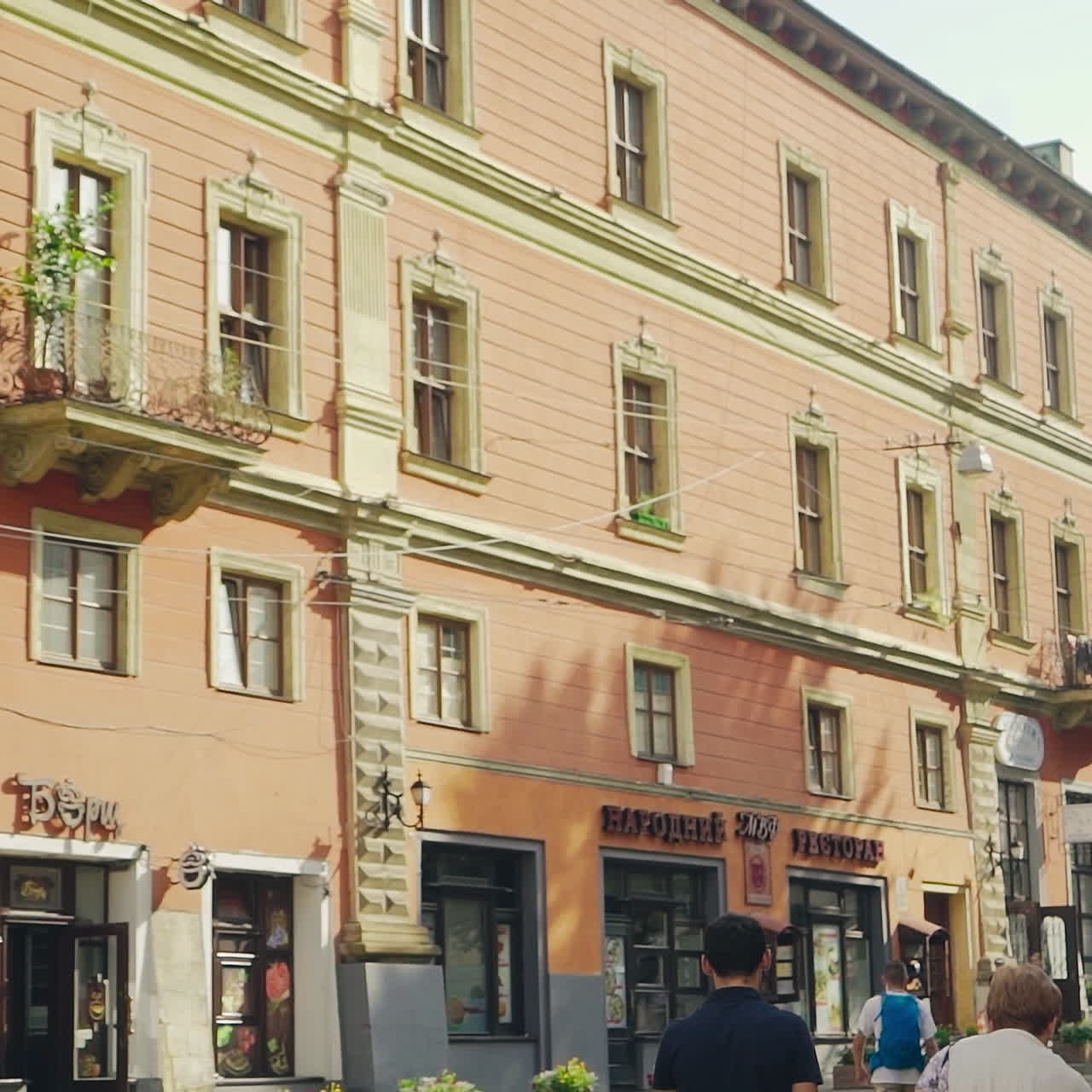 Central city street with ancient buildings and tourists walking on it. People go on the old pavement road in the historical city during the sunny day in summer.