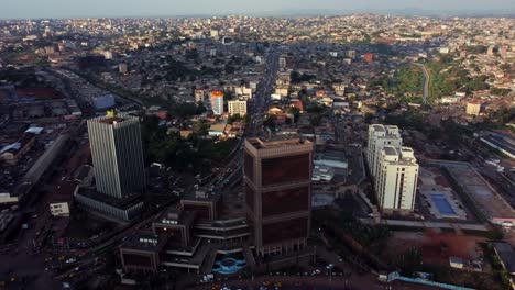 Aerial,-downtown-Yaoundé-office-buildings,-busy-traffic-driving-on-road