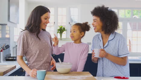familia con dos madres vestidas con pijama haciendo panqueques matutinos en la cocina en casa con la hija