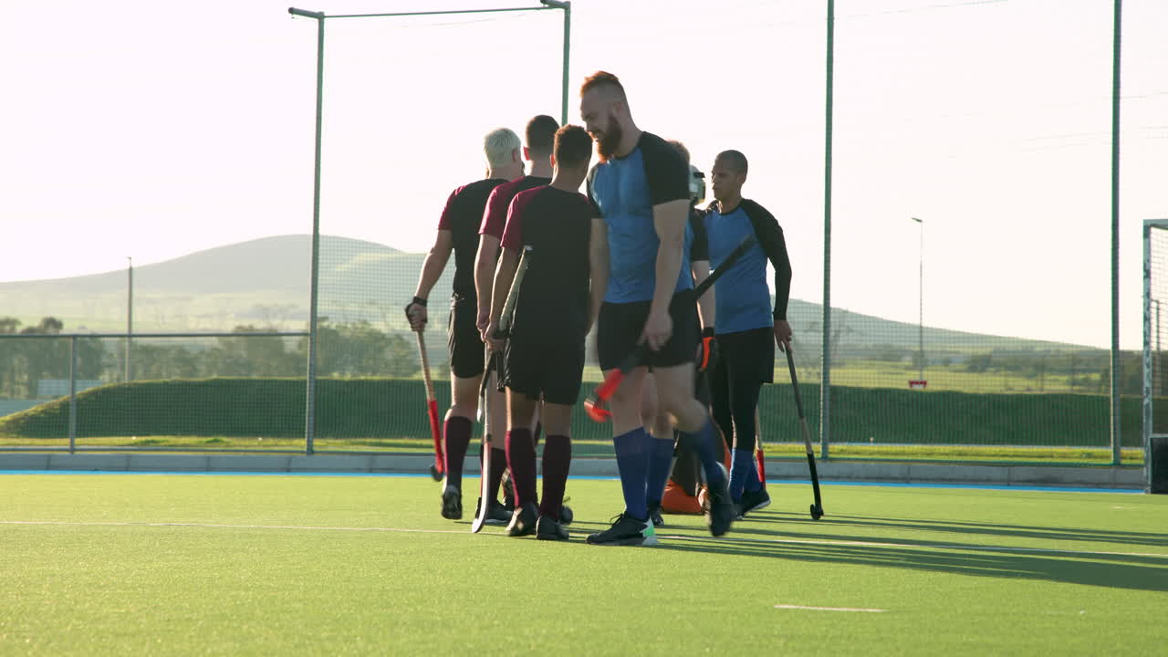 Male hockey players walking on field, carrying sticks and wearing uniforms