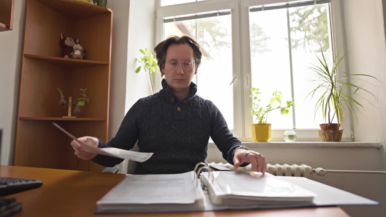 Мужчина в офисе пролистывает большую папку с документами. Ищет документ в пластиковом файле