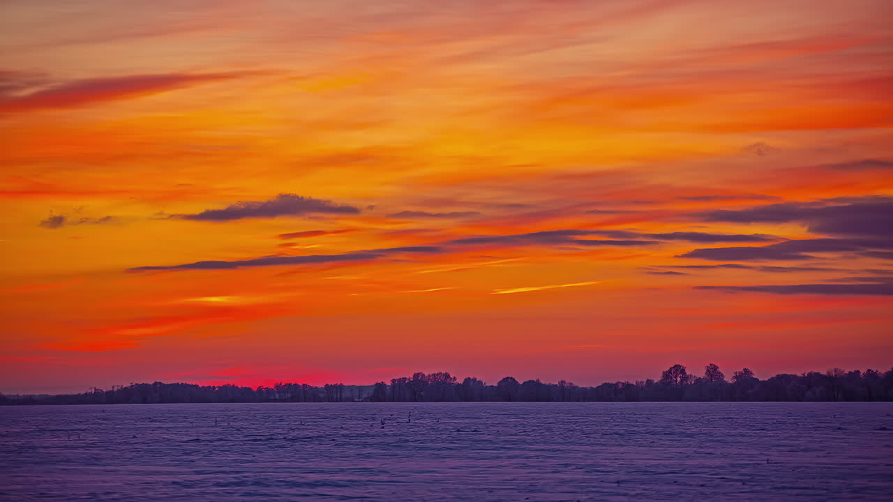 toma de lapso de tiempo del cielo naranja durante la puesta de sol con nubes voladoras sobre el paisaje de invierno blanco