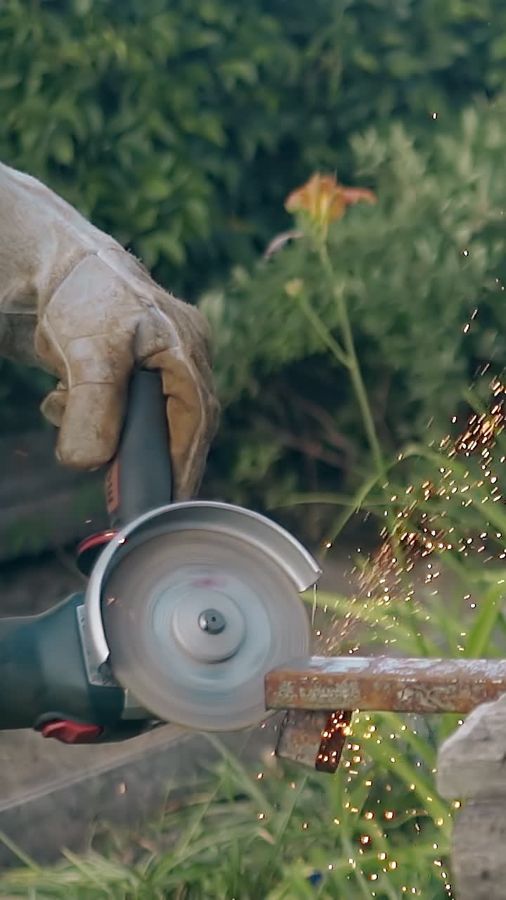 slow motion builder in gloves cuts part of metal detail with circular saw on old table against blooming plants