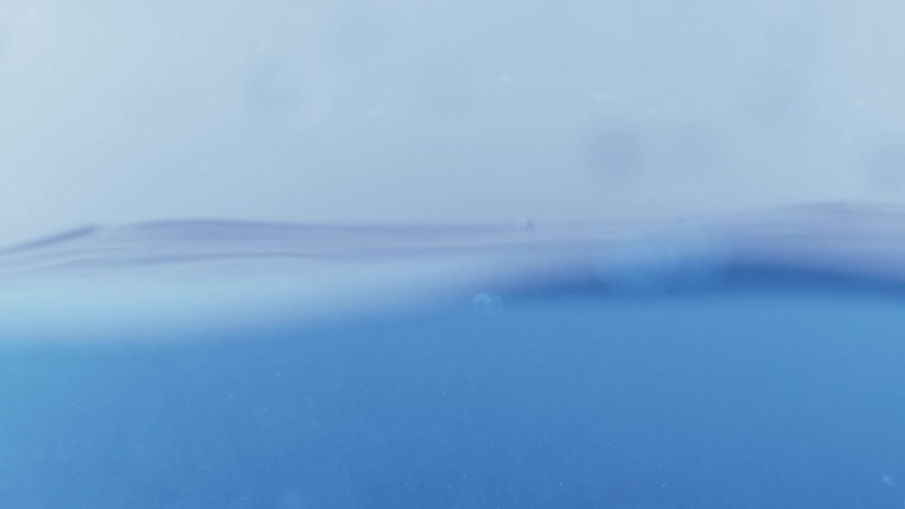 슬로우 모션의 깨끗한 물 표면은 물이 튀는 상점으로 화면을 채우고 기포로 액체 표면을 흔들고 있습니다.