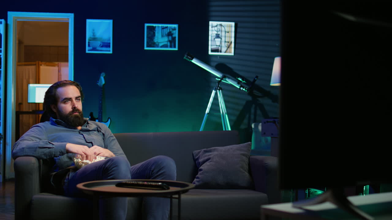 드라마 영화를 보는 동안 스트레스로 인해 소파에서 팝콘을 먹는 슬픈 남자