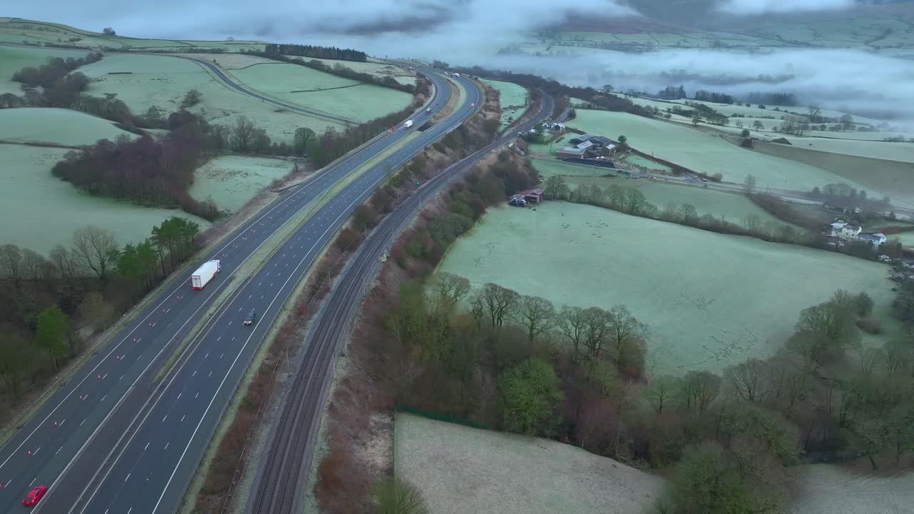 M6 highway with light traffic at dawn in winter with slow pan up revealing fog in shallow valley and low cloud on hills