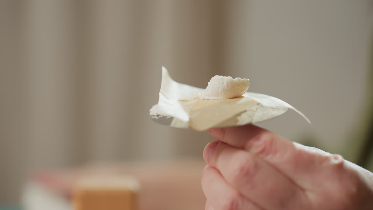 Close up shows icing being placed precisely on cake decorating equipment with swirl candy added on top, while caterer blurred hand is seen in background licking icing from finger during dessert prep