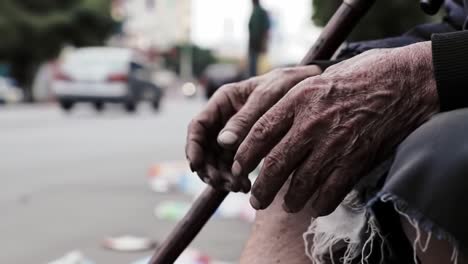 an elderly person holds a cane, hands weathered and dirty, while sitting on a bustling street. people move past without noticing, highlighting the contrast of life and hardship.