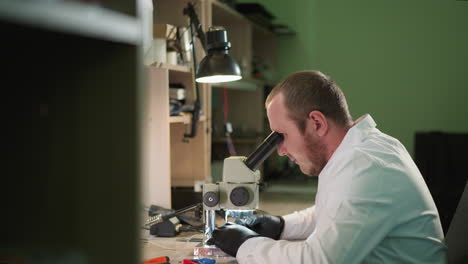 una vista en primer plano de un técnico trabajando meticulosamente en un circuito bajo un microscopio en un laboratorio, luego relajándose, el espacio de trabajo está equipado con una lámpara de escritorio y varias herramientas