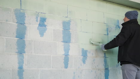 slow motion, painter man with roller painting in white wall in outdoors on cold day