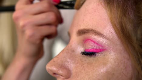 Unrecognizable-makeup-artist-work-in-beauty-studio.-Woman-applying-tone-using-brush.-Artist-make-a-makeup-for-redhead-model-with-freckles.-Close-up-of-a-pretty-girl-with-pink-eye-shadows