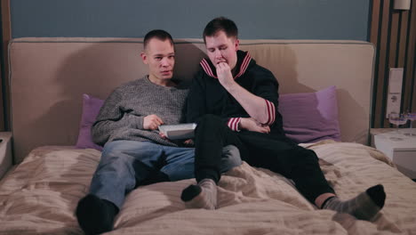 two men relaxing and eating in a bedroom