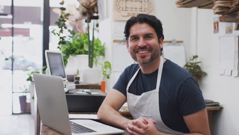 portrait of male sales assistant working on laptop behind sales desk of florists store