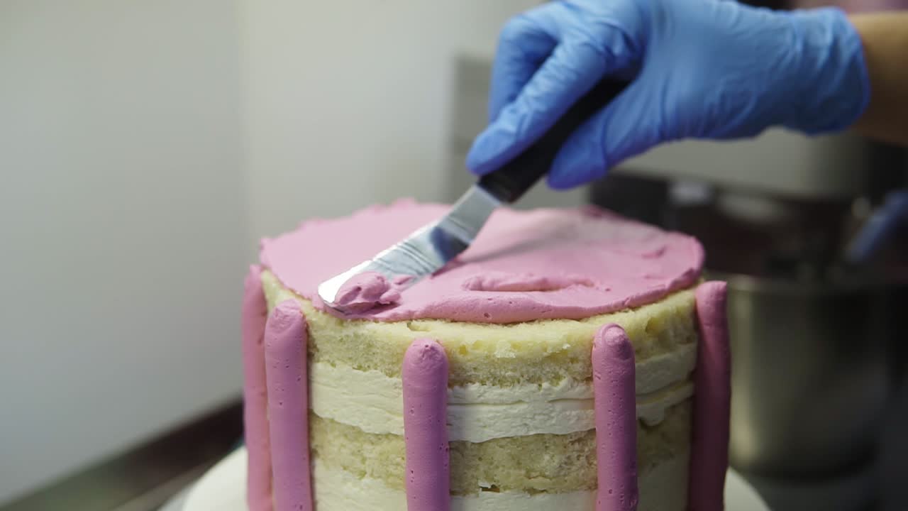 Confectioner applying puprle whipped cream on top of biscuit cake equating it with pastry spatula. Creating delicious cake. Food art.