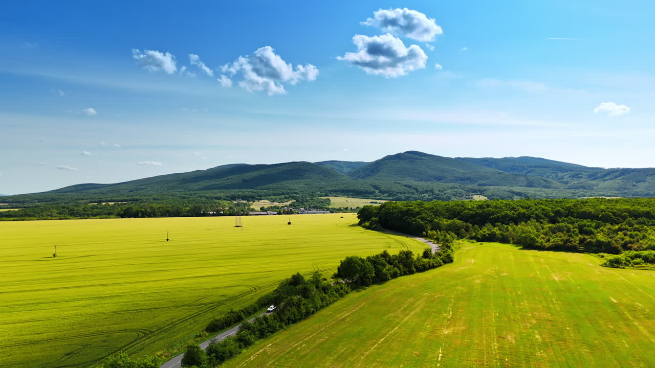 Vast green fields beneath a blue sky. Lush green fields stretch across the landscape, bordered by rolling hills and a bright blue sky with clouds