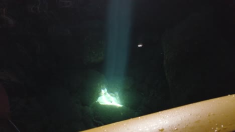 Kayaker-observing-a-beam-of-light-reflecting-on-some-rocks-in-the-water-inside-a-sea-cave,-Vis-island,-Adriatic-Sea,-Croatia