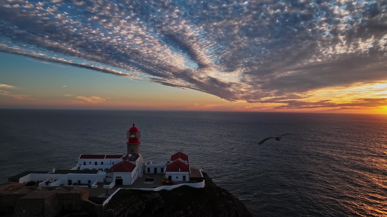 A close-up aerial view of the lighthouse with soft sunset light illuminating its red top.