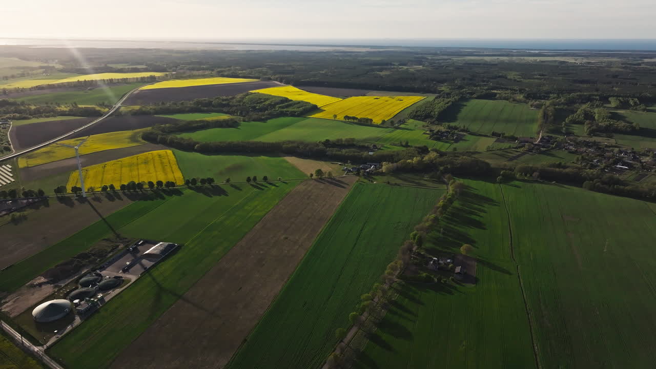 Drone pans across colorful farmlands with wind turbines generating green energy, rural peaceful backdrop with shadow