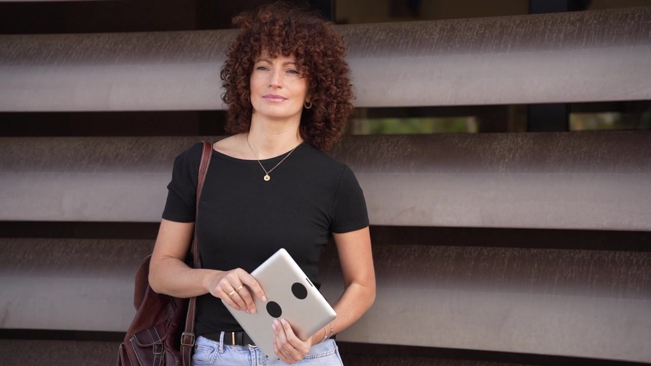 Una donna con bellissimi capelli ricci usa un tablet mentre si gode l'aria aperta in un contesto cittadino