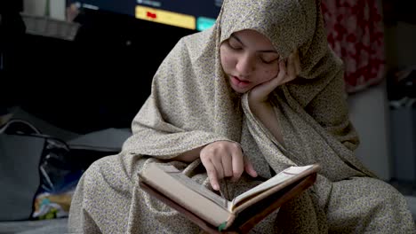 Devout-young-Indian-female-Muslim-sits-quietly-reciting-Quran-in-public-area-MEDIUM-SHOT